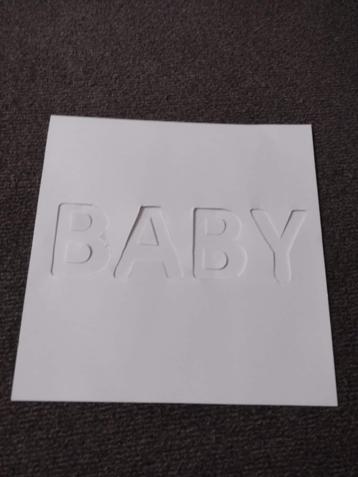 Picture of strip of paper backing a piece of paper with the word "baby" cut out
