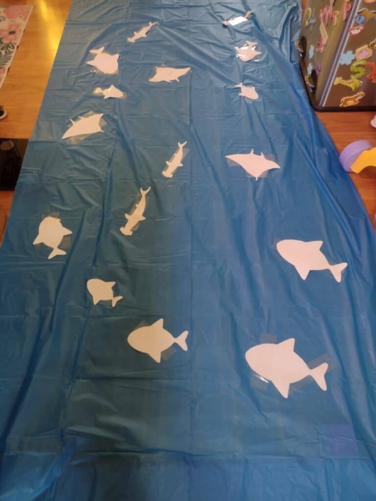 Picture of paper fish, sharks, and stingrays taped to a blue tablecloth