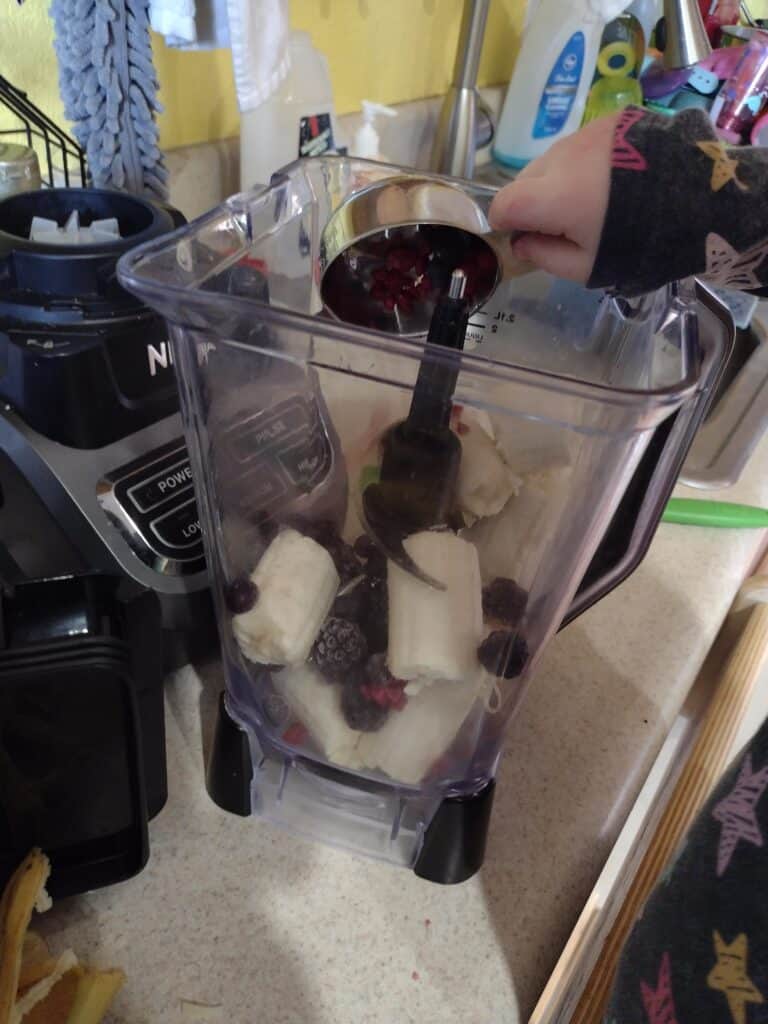 Picture of a preschooler pouring a scoop of frozen berries into a blender