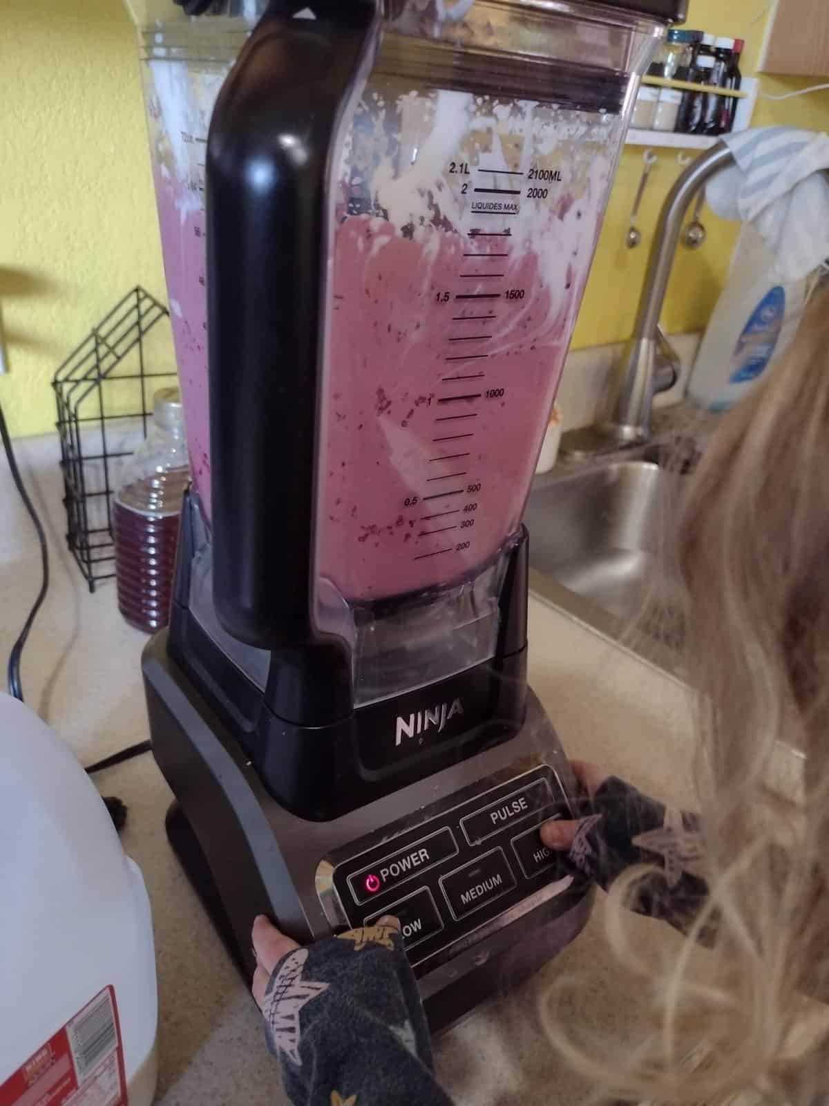 Picture of a preschooler pressing buttons on a blender to make a smoothie