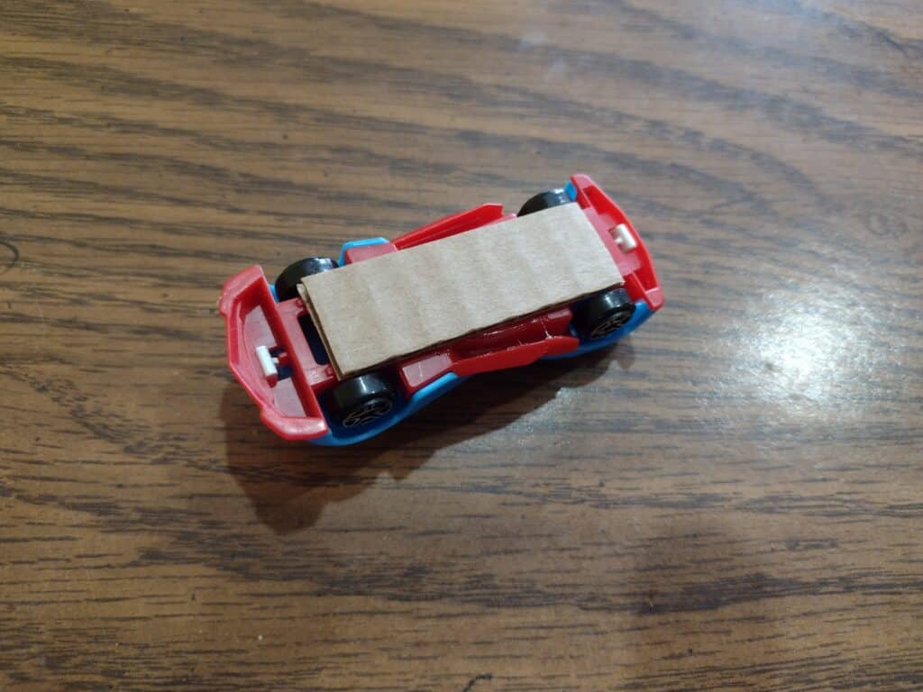 Picture of a strip of cardboard hot glued to the bottom of a matchbox car