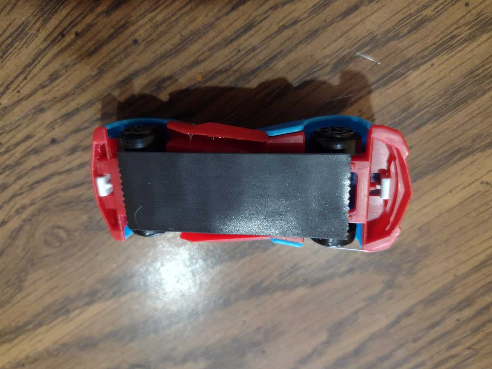 Picture of a piece of magnetic tape stuck to a piece of cardboard glued to the bottom of a matchbox car