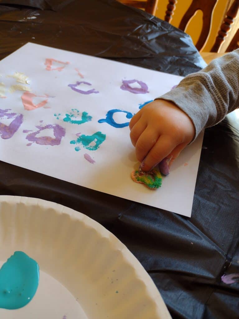 Picture of a preschooler stamping a heart shaped pipe cleaner covered in paint onto a piece of paper
