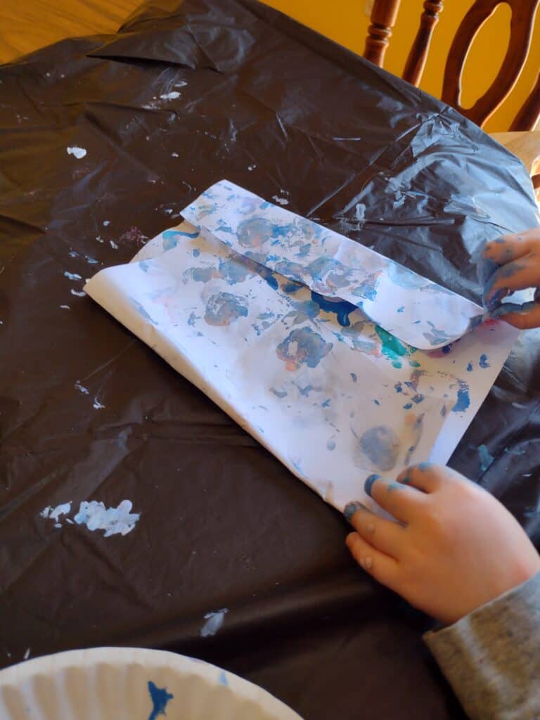 Picture of a preschooler folding a piece of paper with paint shapes over