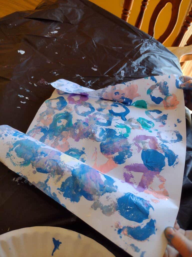 Picture of a toddler unfolding a piece of paper with wet paint on it