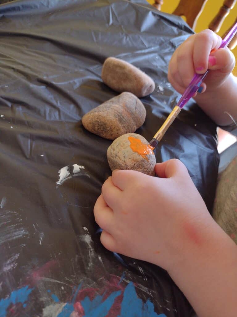 Picture of a preschooler painting a rock orange