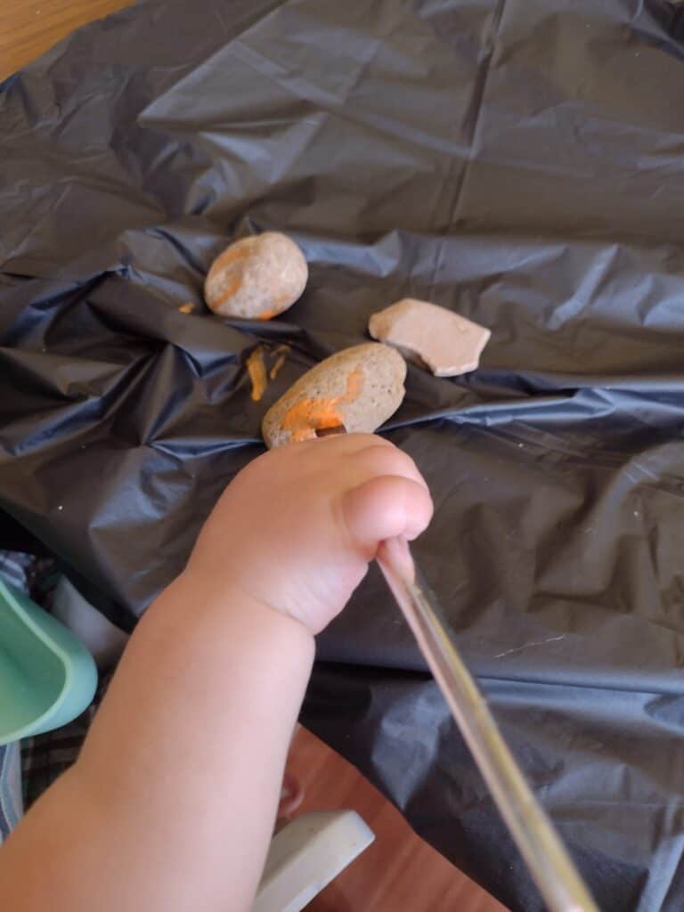 Picture of a toddler painting a rock orange