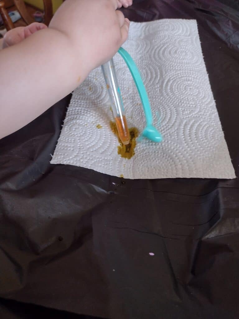 Picture of a toddler dropping yellow food dye on a paper towel