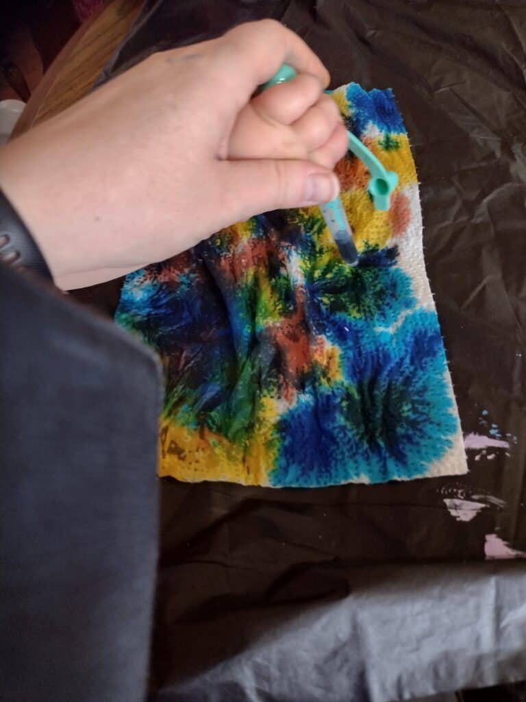 Picture of a toddler yellow food dye on a paper towel with an adult's help