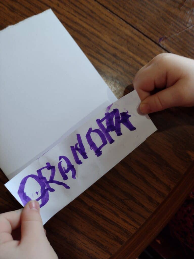 Picture of a preschooler placing a strip of paper saying Grandpa on the bottom of a blank card