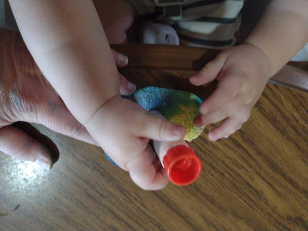 Picture of a toddler using a glue stick on the back of a paper towel tie dye heart