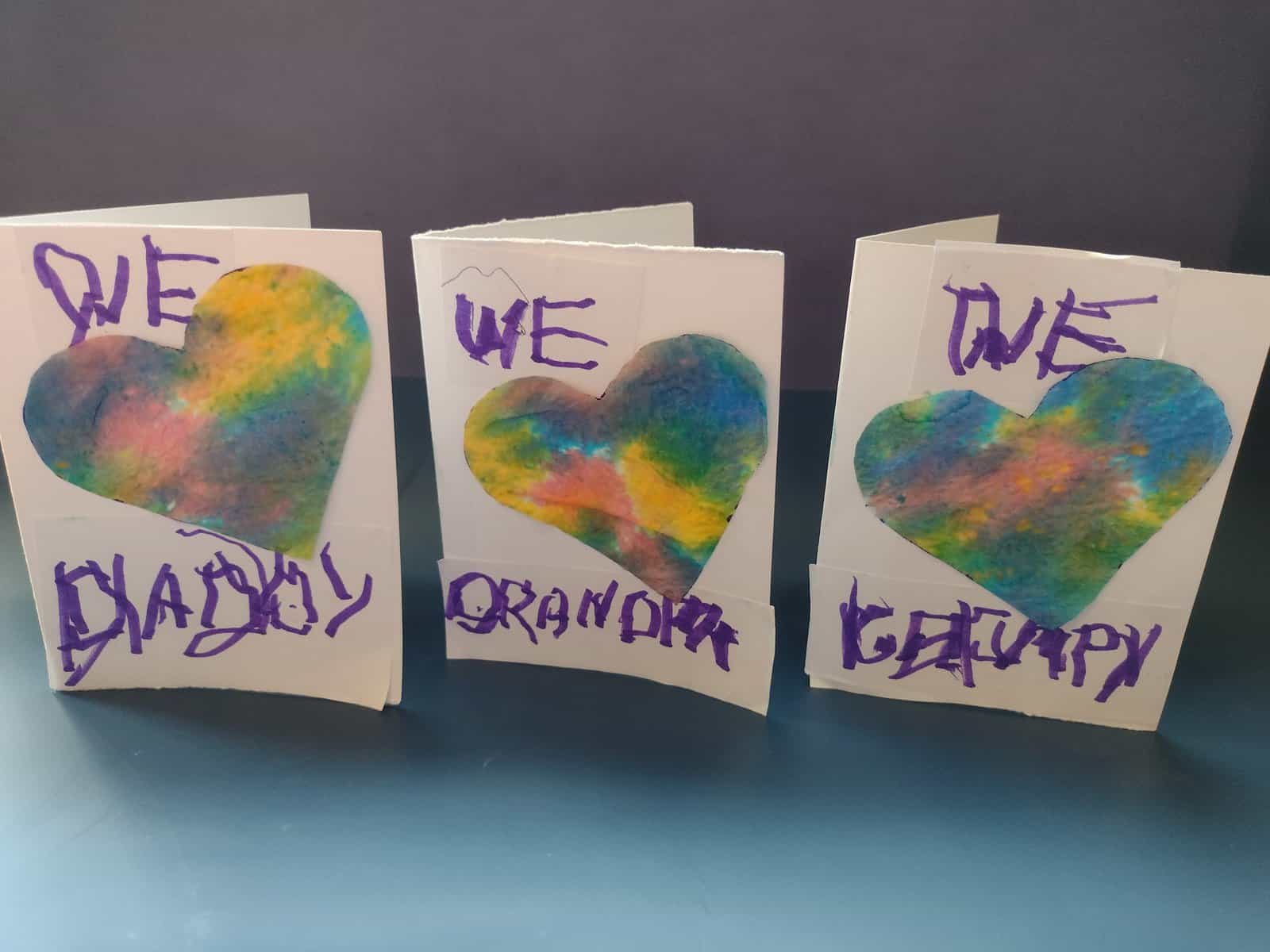 Picture of homemade Father's day cards that say "We love Daddy" "We love Grandpa" and "We love Grumpy". The love is a heart made from tie dye paper towel.