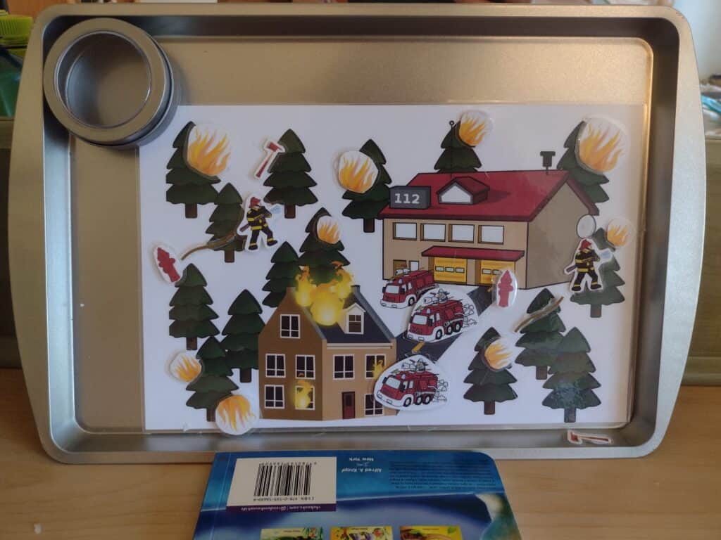 Picture of a firefighter play mat propped up vertically with just a few firefighter pieces fallen off and laying on the rim