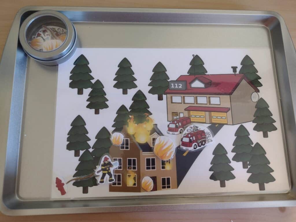 Picture of firefighter playmat with some firefighter pieces stuck to it and some in a magnetic container off to the side