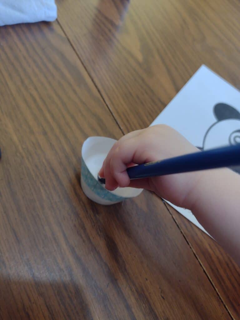 Picture of a preschooler dipping a pencil with a tissue paper square on the end into a cup of glue