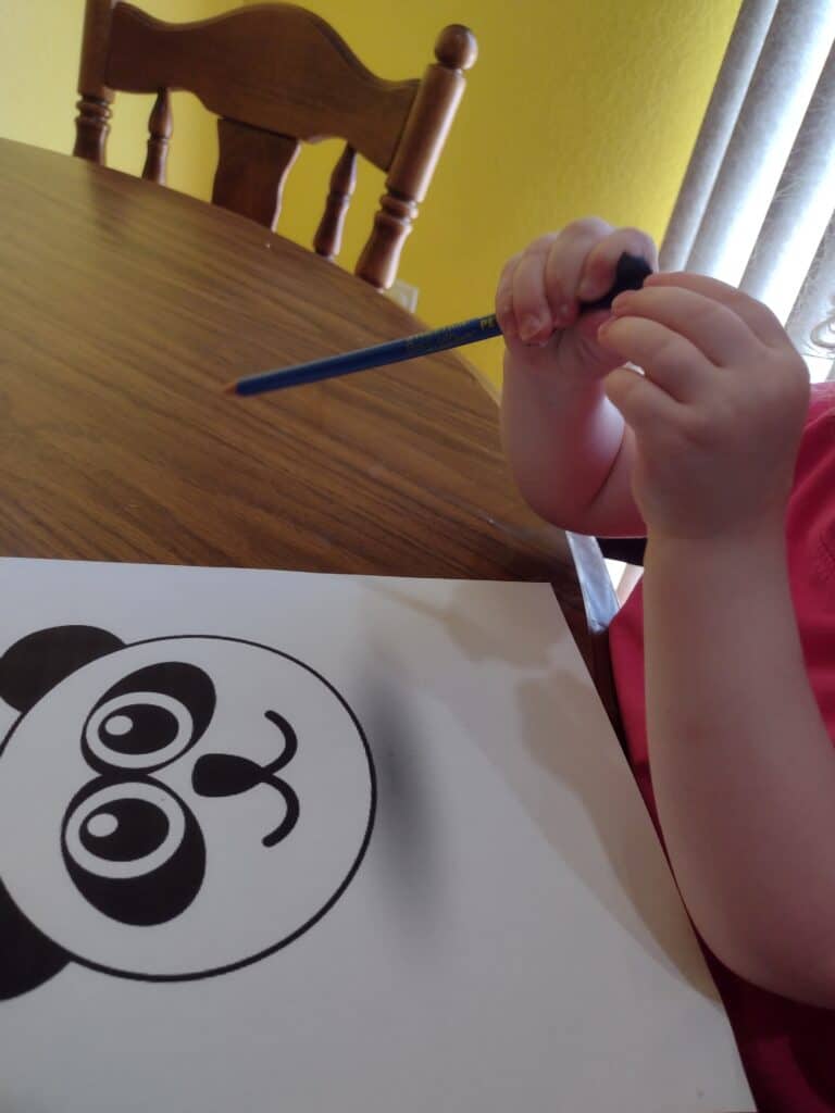 Picture of a preschooler wrapping a black square of tissue paper around a pencil