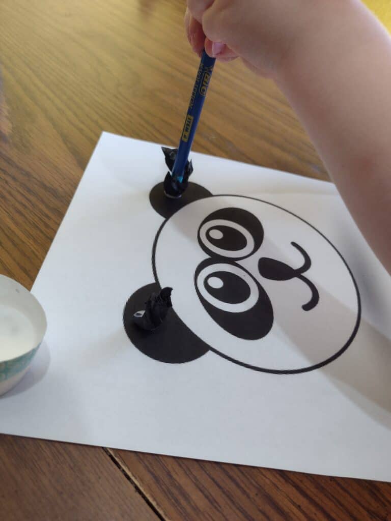 Picture of a preschooler gluing black tissue paper onto a panda craft using the end of a pencil