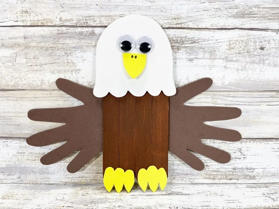 Picture of a bald eagle craft with its body made from popsicle sticks and its wings from handprints