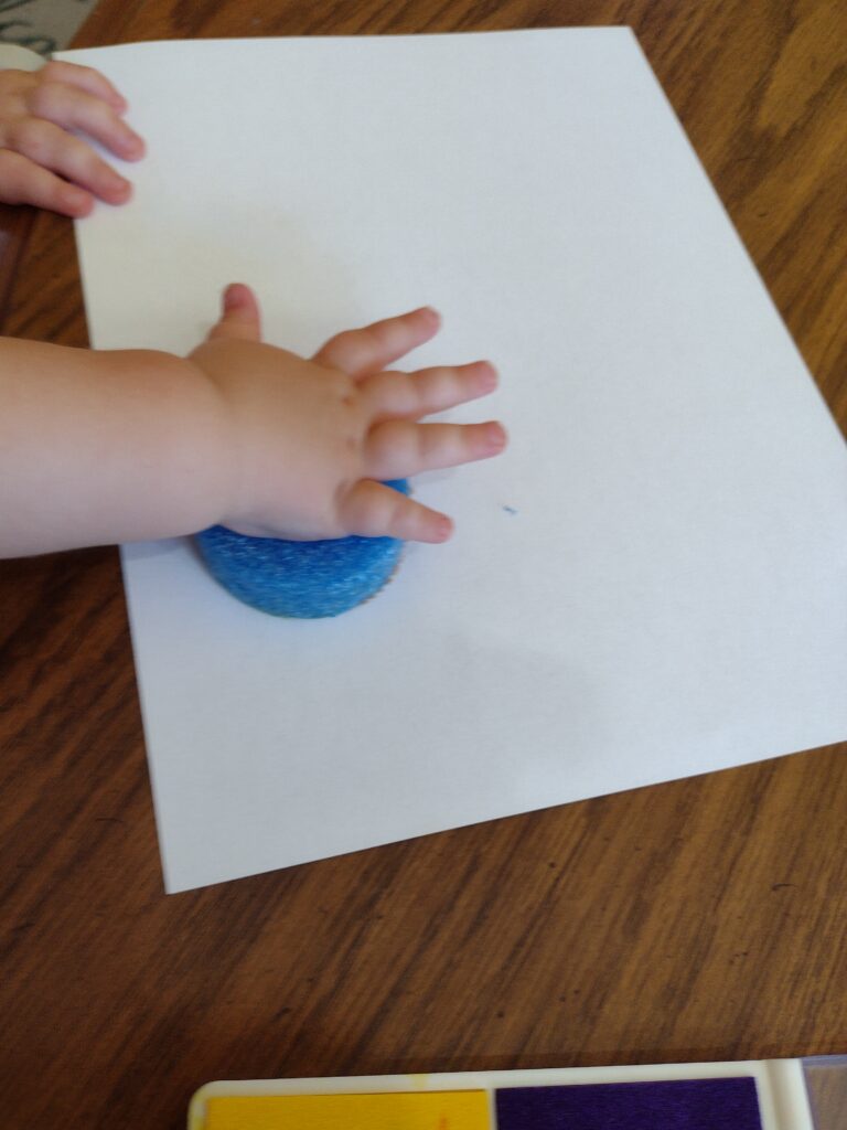 Picture of a toddler pressing a handmade stamp onto a piece of paper