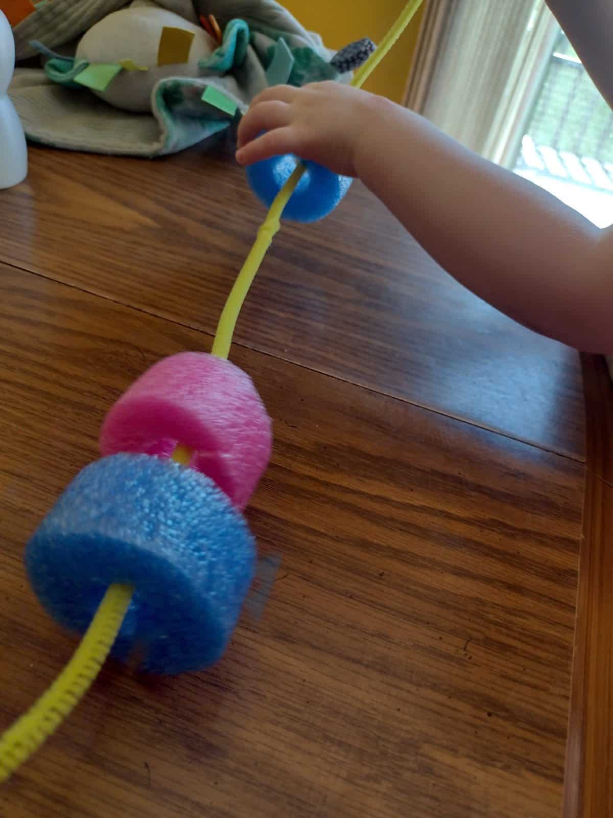 Picture of a preschooler threading a piece of a pool noodle onto a pipe cleaner