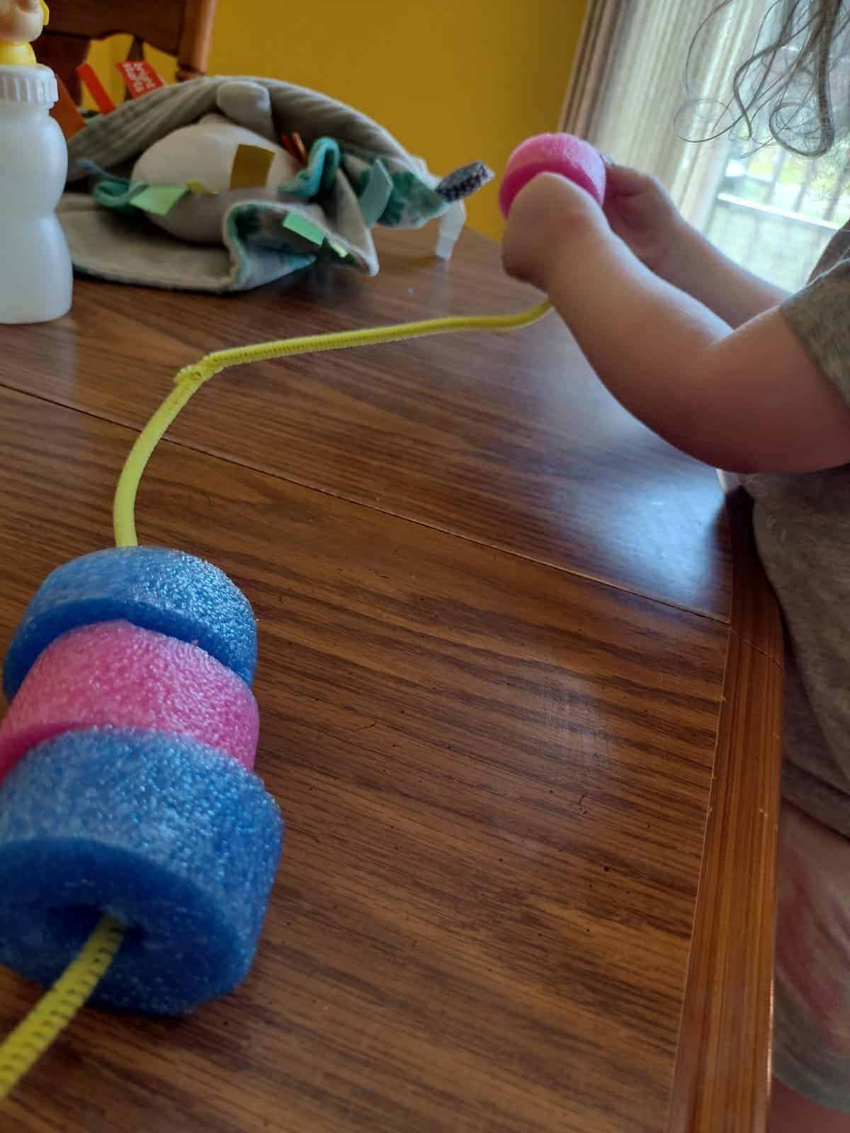 Picture of a preschooler threading a piece of a pool noodle onto a pipe cleaner