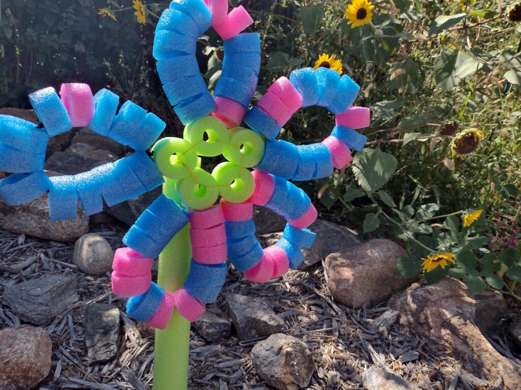 Picture of a flower shaped pool noodle craft placed in front of sunflowers
