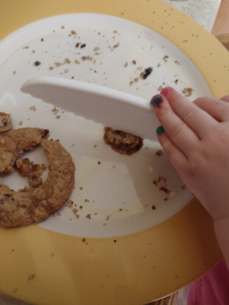 Picture of a preschooler cutting a small circle of oatmeal cookie in half