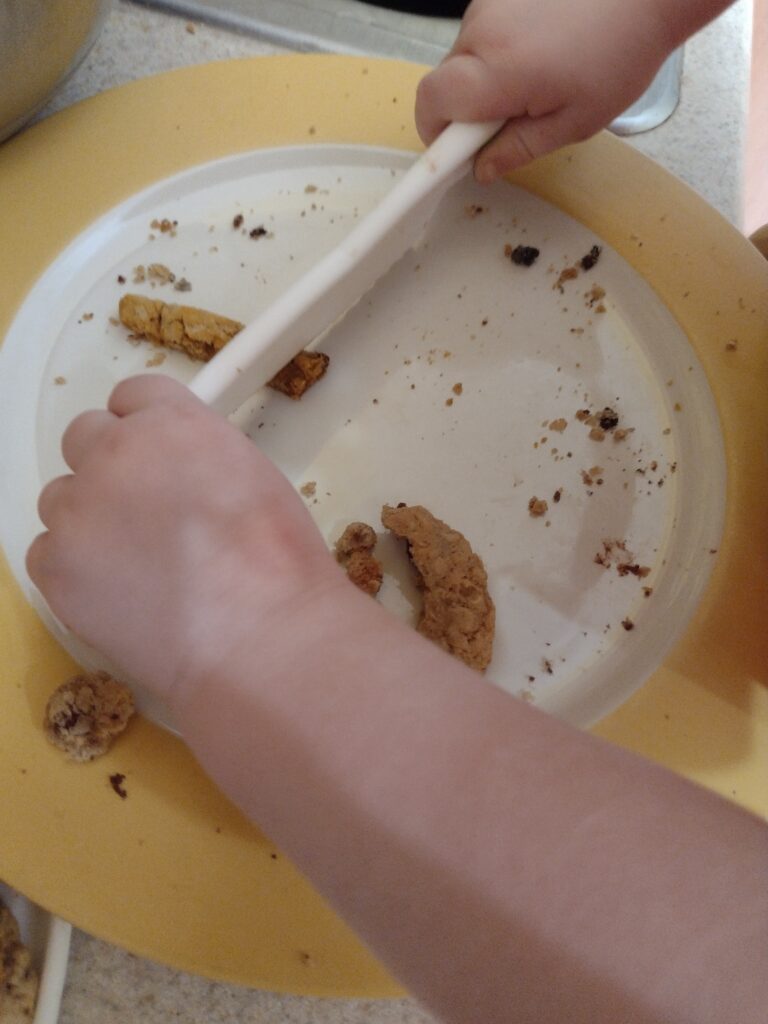 Picture of a preschooler cutting small triangles off of an orange colored oatmeal cookie