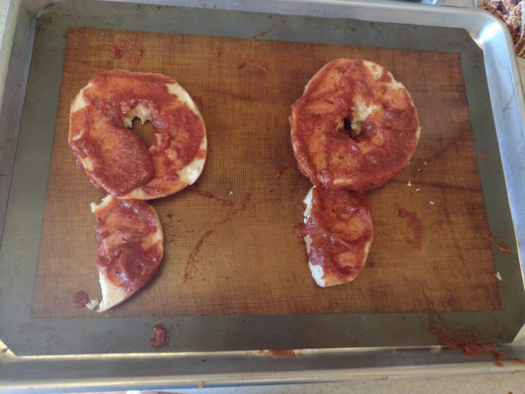 Picture of two P shaped bagels covered in pizza sauce