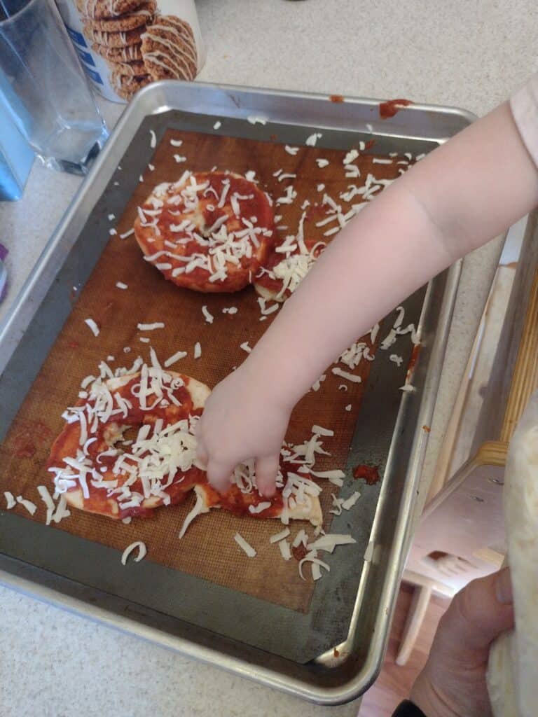 Picture of a preschooler spreading cheese on a P shaped bagel pizza