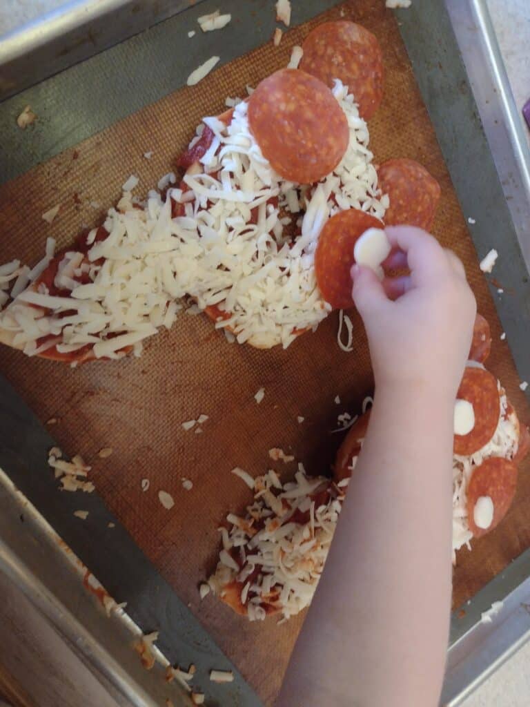 Picture of a preschooler placing a slice of a cheese stick as the eye of a panda onto a pizza