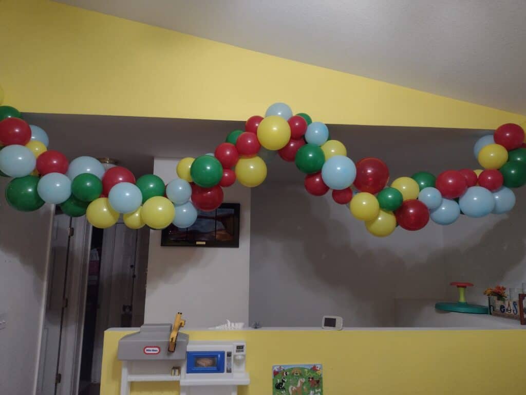 Picture of a balloon arch hanging on the wall. The balloons are red, green, yellow, and blue.