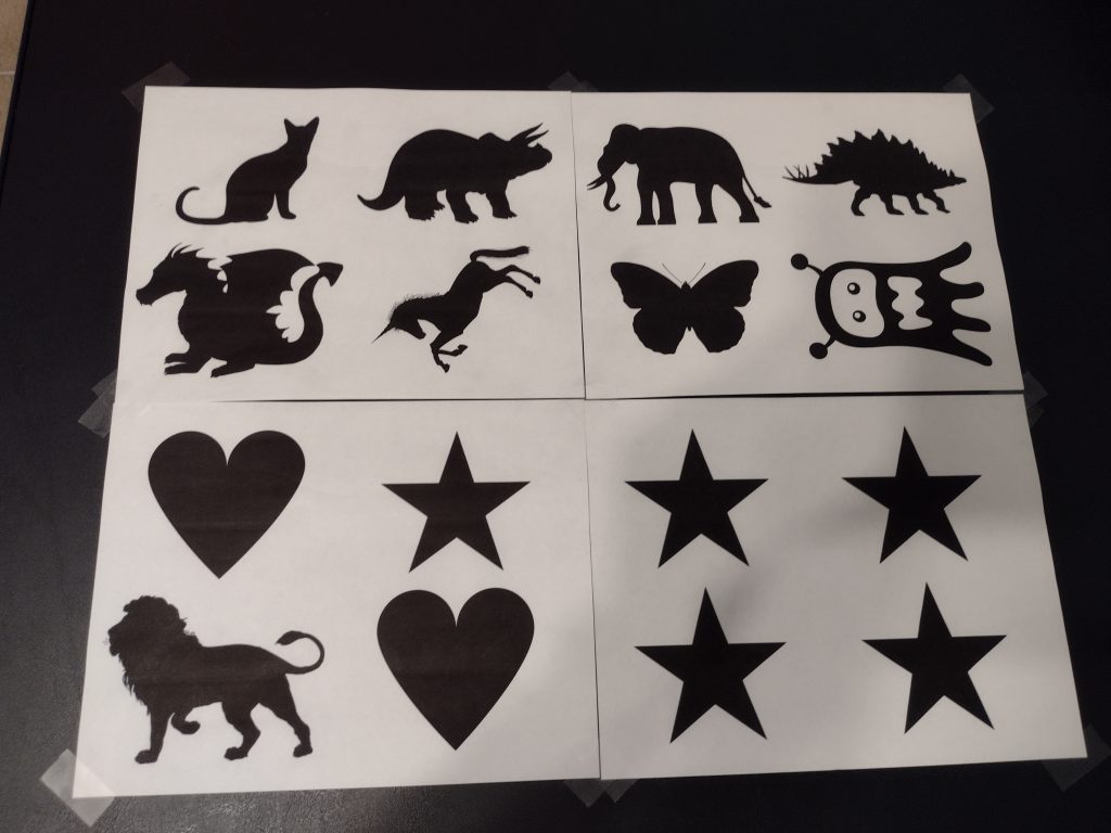 Picture of printed sheets of the silhouettes of a cat, dinosaurs, an elephant, a dragon, an unicorn, a butterfly, a monster, a lion, hearts, and stars