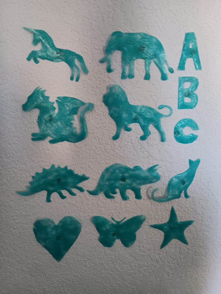 Picture of DIY glow in the dark stars, an unicorn, an elephant, alphabet letters, a dragon, a lion, two dinosaurs, a cat, a heart, and a butterfly. 