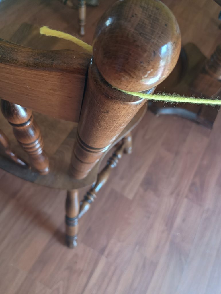 Picture of one end of a skein of yellow yarn tied to a chair