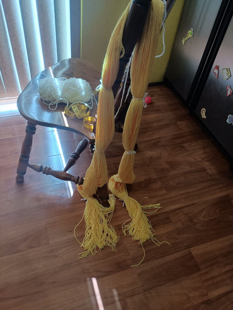Picture of an entire skein of yellow yarn looped around two chairs and tied with white yarn every so often and cut on one side