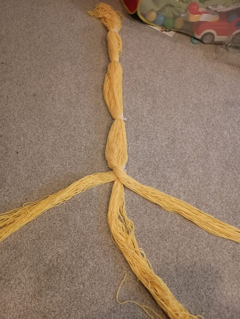 Picture of a large bunch of yellow yarn separated into three strands starting in the middle of the bunch