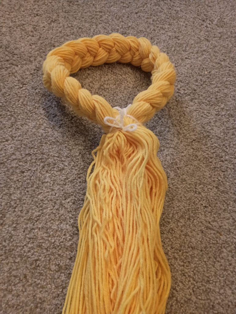 Picture of braided yellow yarn tied in a loop with a bunch of loose yellow yarn hanging down