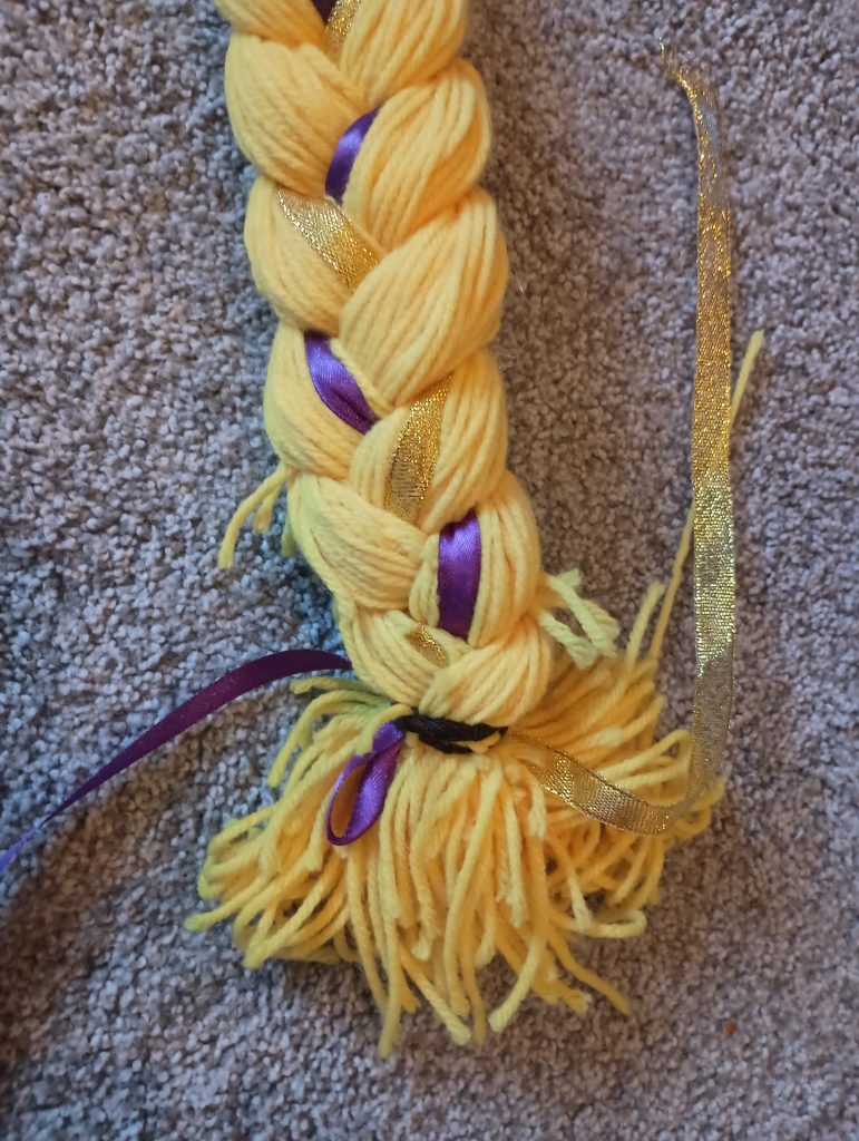 Picture of the bottom of a Rapunzel hair braid. The ends are messy and pieces of yarn are sticking out from the braid