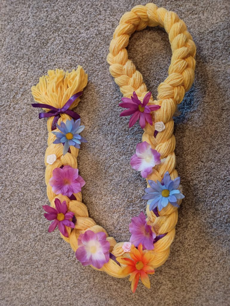 Picture of yellow yarn braided to make a Rapunzel hair costume wig. There are fake flowers glued all over the braid