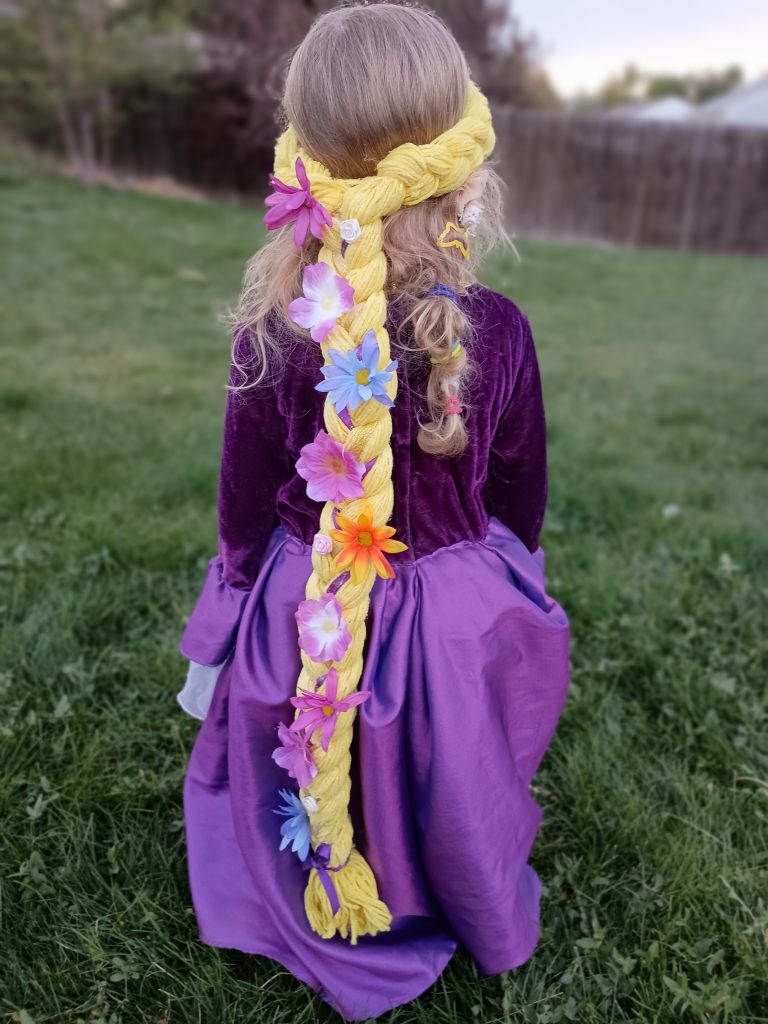 Picture of the back of a preschooler wearing a Rapunzel dress and a DIY Rapunzel braid made from yellow yarn